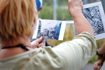 Kobieca postać trzyma w dłoniach reprodukcje archiwalnych zdjęć z okolicy obecnego ronda Lotników Polskich